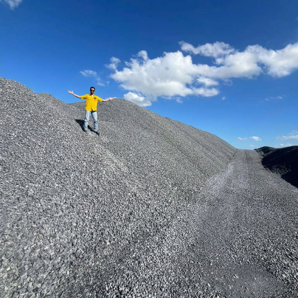 Sonny's Rio Rock-N-Stone team member in a branded shirt standing atop a massive crushed aggregate stockpile, showing the scale of supply